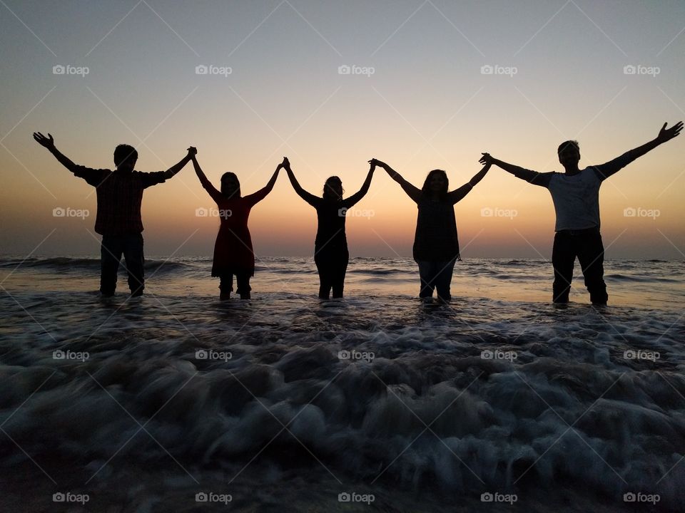 Friends standing in sea with hands raised
