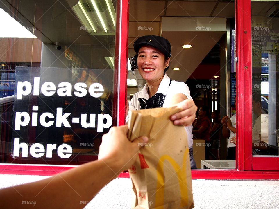 a fastfood restaurant worker hands over a customer his order at a drive thru window