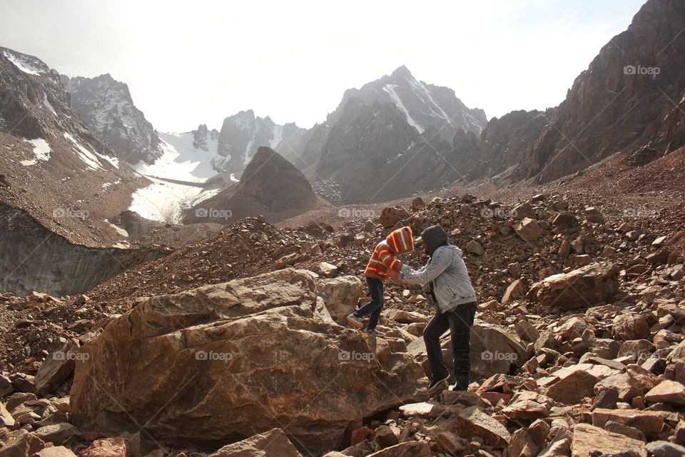 Dad helps little daughter climb down a cliff in the mountains on a glacier