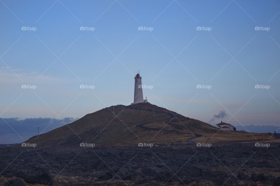 White lighthouse on a hill in Iceland with a S-curve way leading up during the blue hour.