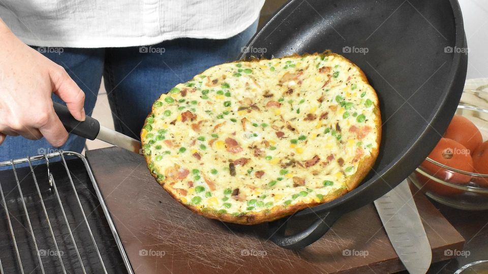 Homecooking cooking Frittata at home and adding and mixing ingredients and removing the Frittata from the pan for cutting and serving on a white plate with tomatoes. Healthy home cooking in kitchen. Breakfast and lunch food preparation. 