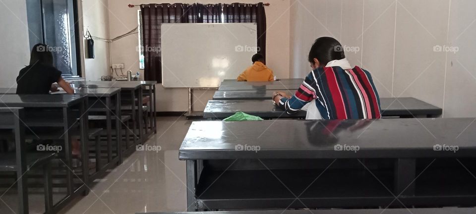 Photo image of is in classroom of college. Students are busy in writing.