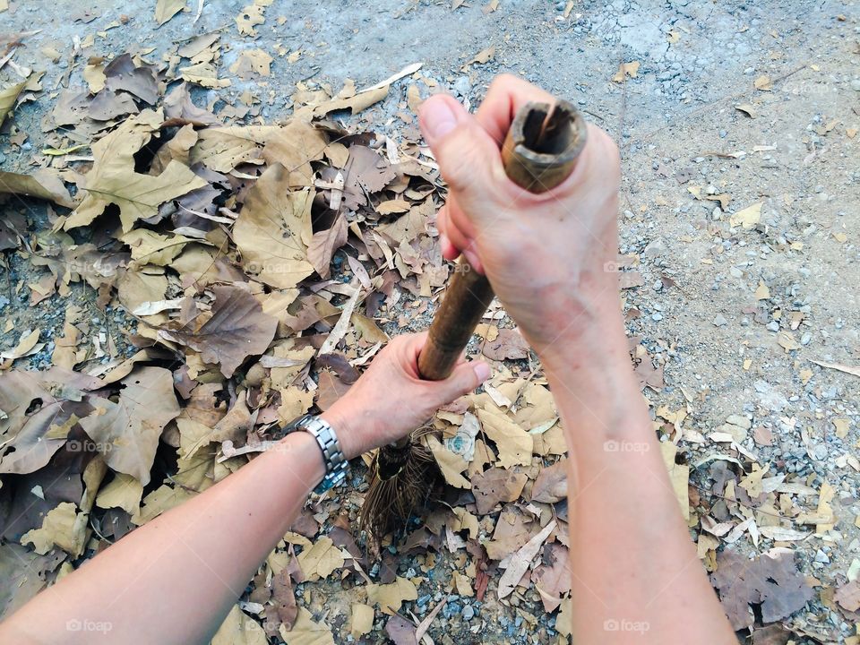 female hand hold bamboo broom to clean dry leaves in autumn season