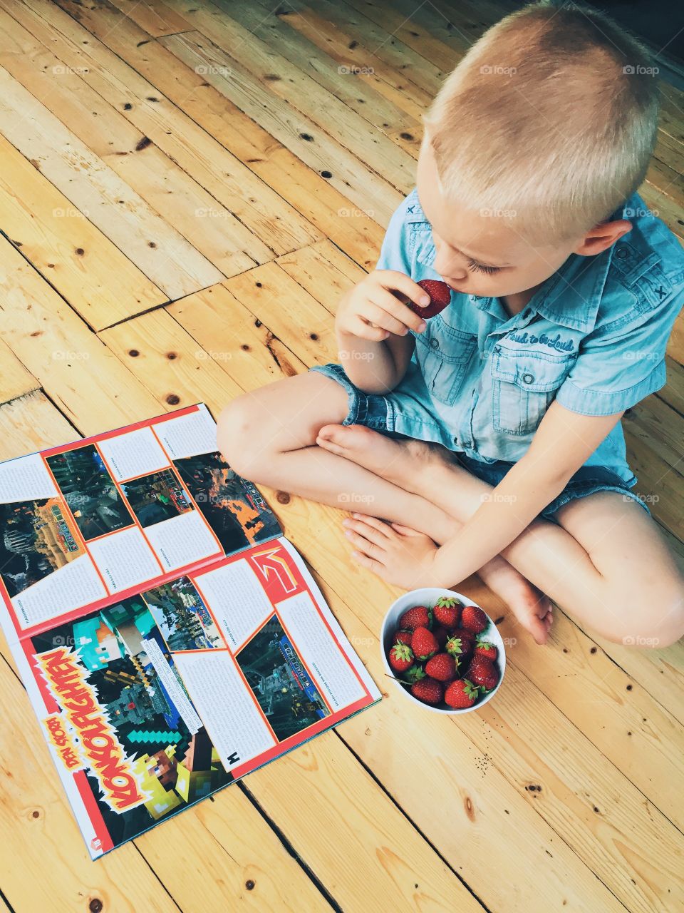 Boy eating strawberries and reading a magazine