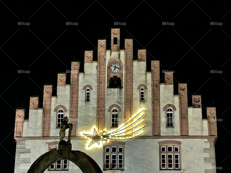 Illuminated Christmas star on the town hall in Hammelburg by night with the figure from a fountain in front of it.