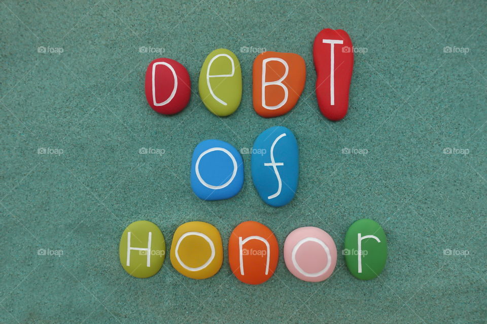 Debt of honor, creative text composed with multi colored stones over green sand