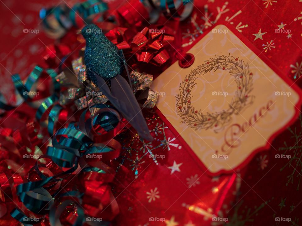 A decorative blue bird with glitter amongst colorful ribbon on a wrapped Christmas present. 