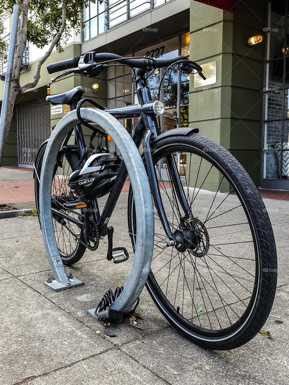 Black bicycle chained up on the streets of San Francisco, sleek with the safety helmet strapped to its side 