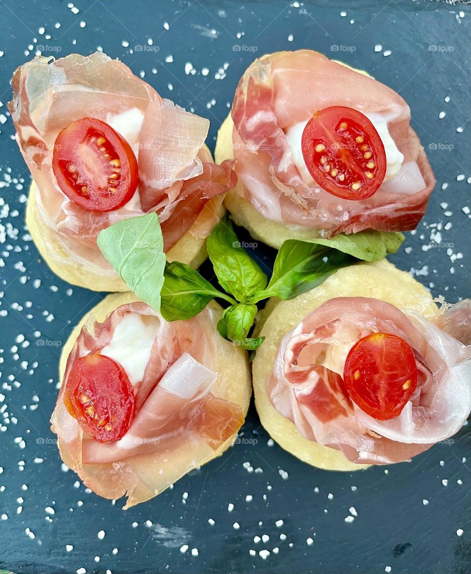 Typical colorful Italian appetizers made with pizza dough, ham, cherry tomatoes, basil and a sprinkle of flaky fleur de sel salt  