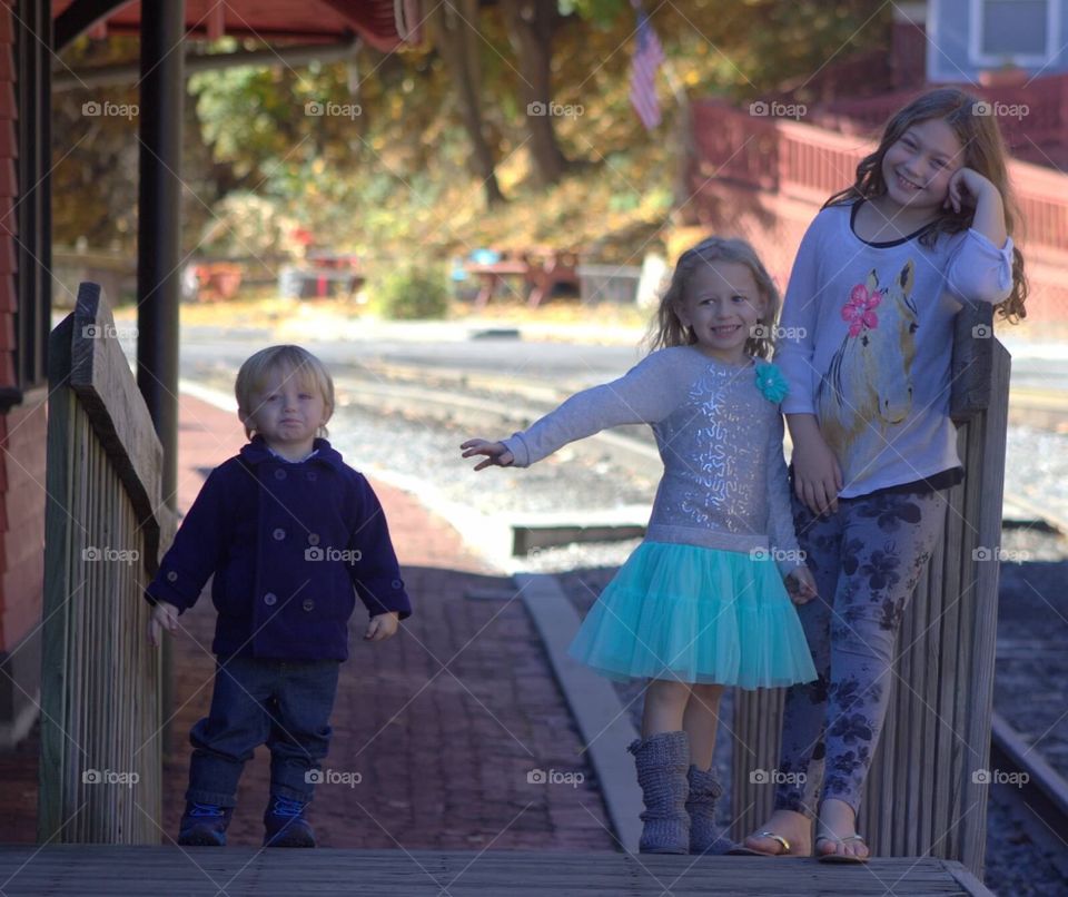 Three adorable siblings playing around at the train station. 
