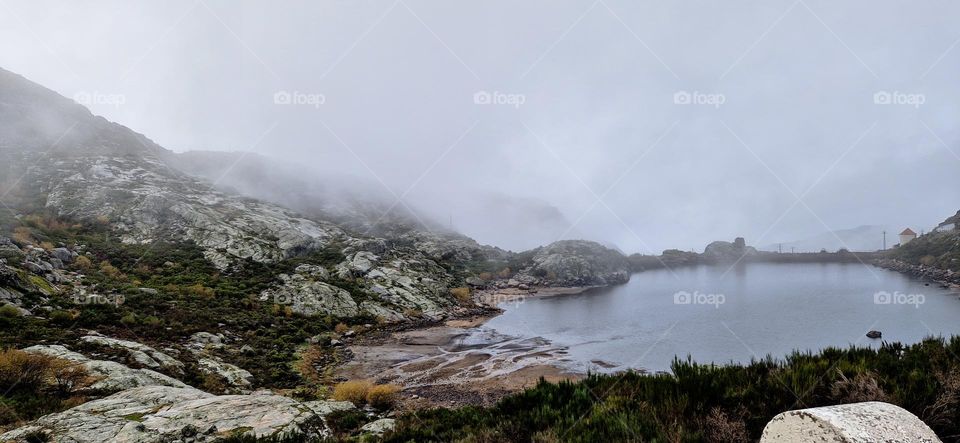 Small lake in the middle of the rocky mountains in Serra da Estrela, Portugal. Mountains surrounded by the fog.