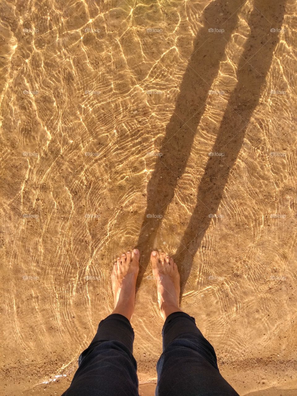 female legs barefoot in the water lake sand shore and shadows, abstract background, spring time