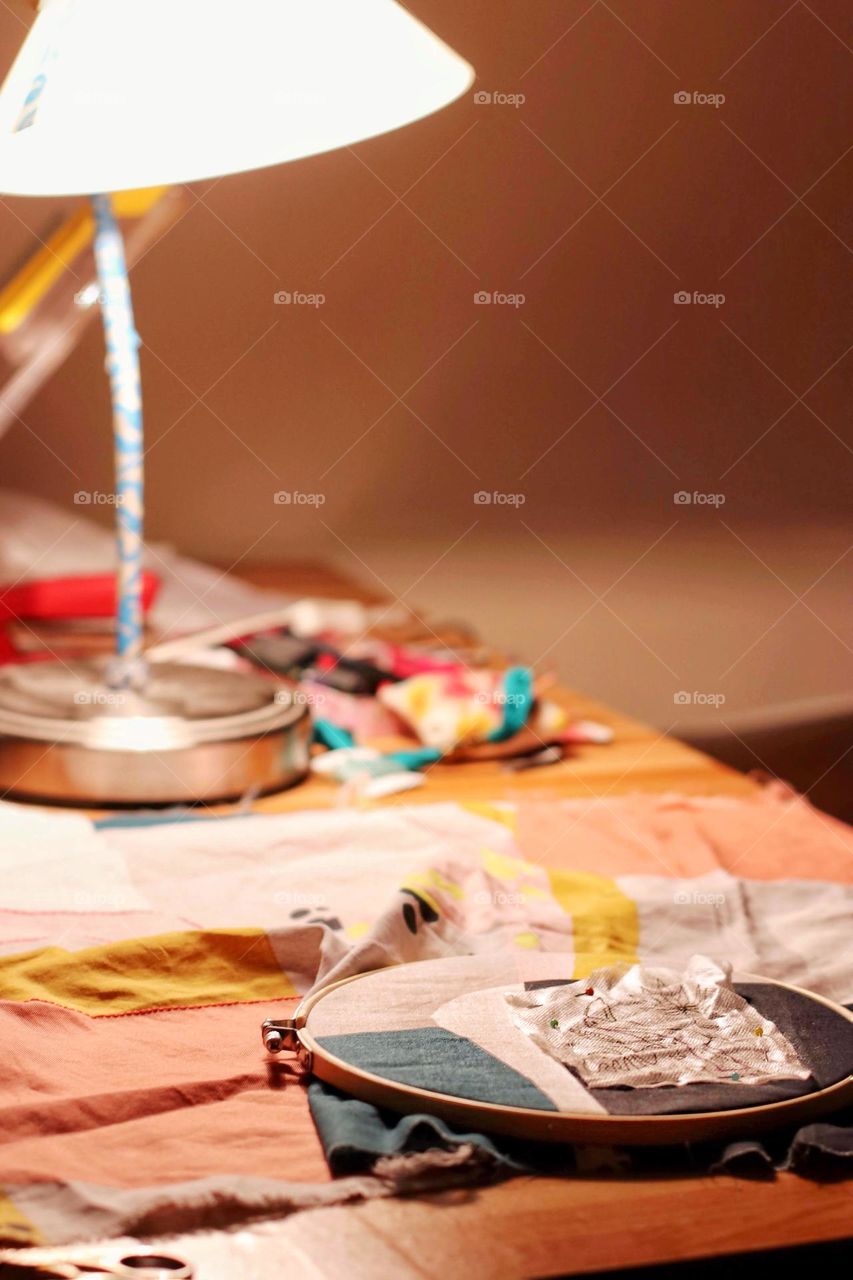 View of colorful fabrics and embroidery frames with embroidery under a lamp
