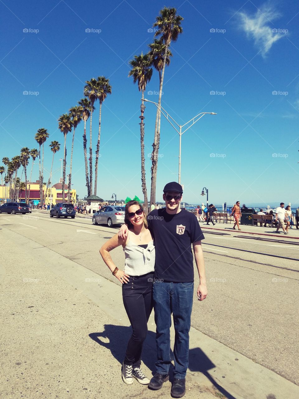 Couple Posing on a Street with Palm Trees and the Beach Behind Them