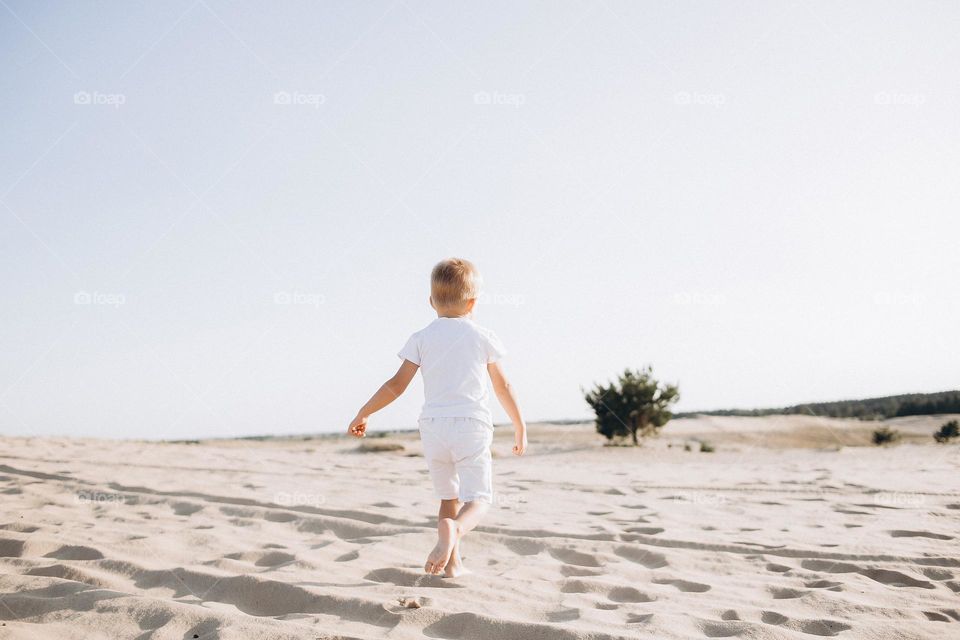 Small boy in white clothes walking in desert