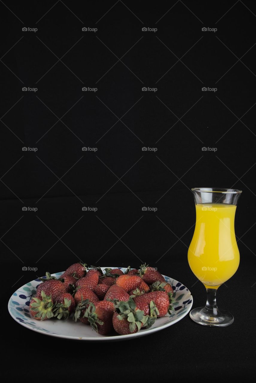 Strawberries with glass of natural juice on black background