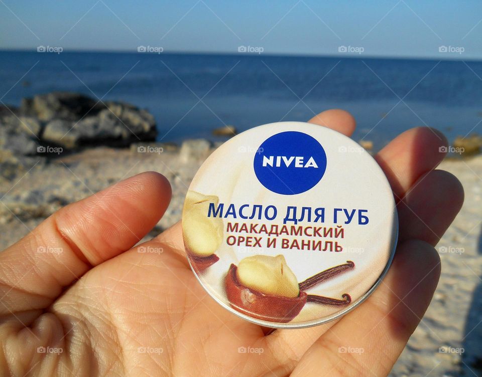 lip balm Nivea in the hand on a sea shore, vacation product