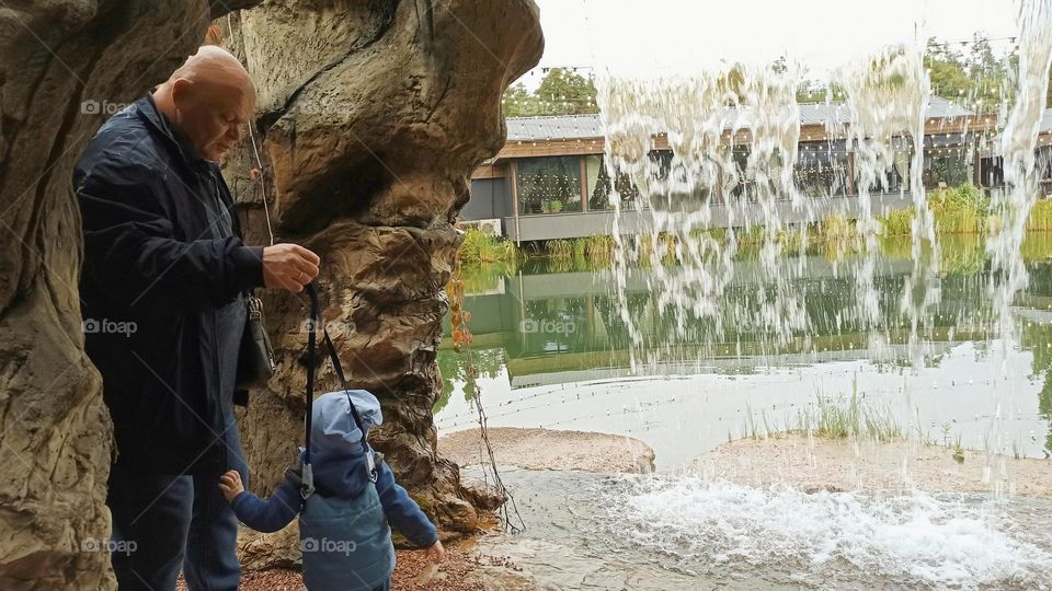 dad holds his son and admire the mini waterfall and nature