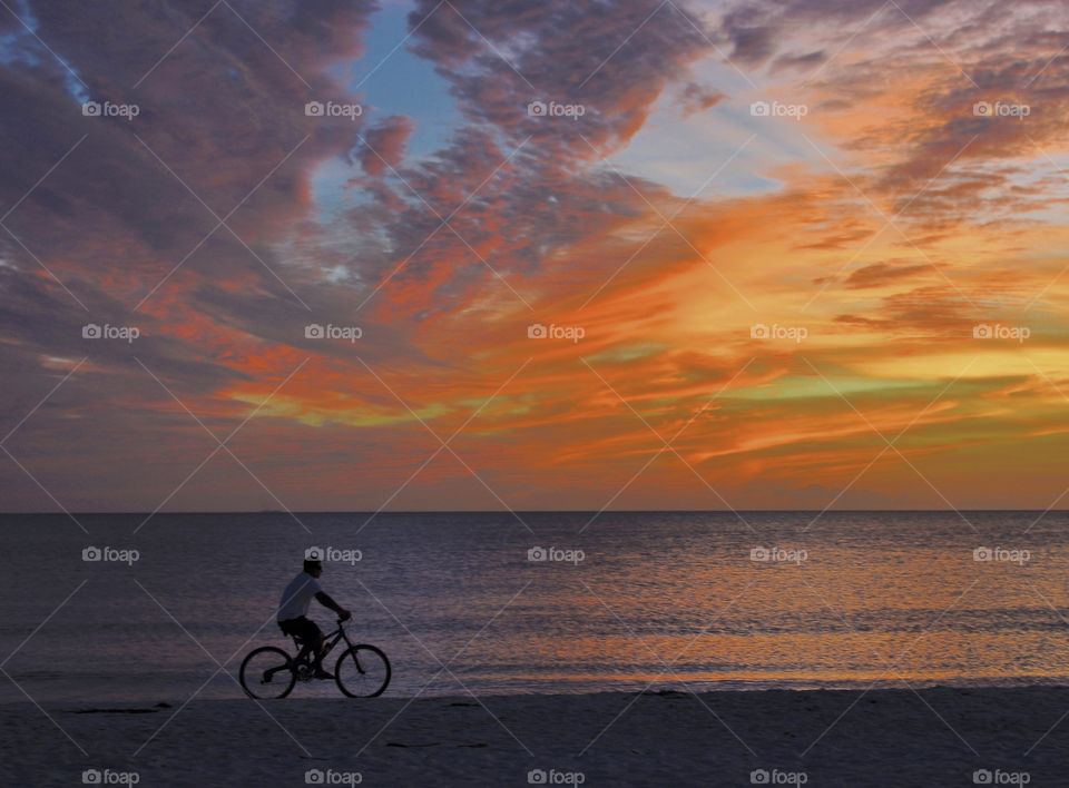 Sunset, person riding bike on the beach 