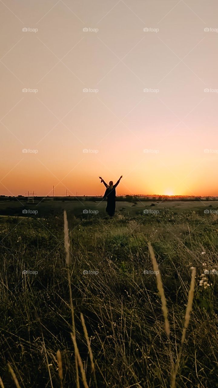 Woman's dark silhouette on the horizon line in the field. Meditation on sunset, deep connection with nature