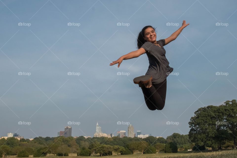 Foap, Best of the Best: An exuberant young girl leaps into the air, rising above the city skyline as seen Dorothea Dix Park in Raleigh North Carolina. 