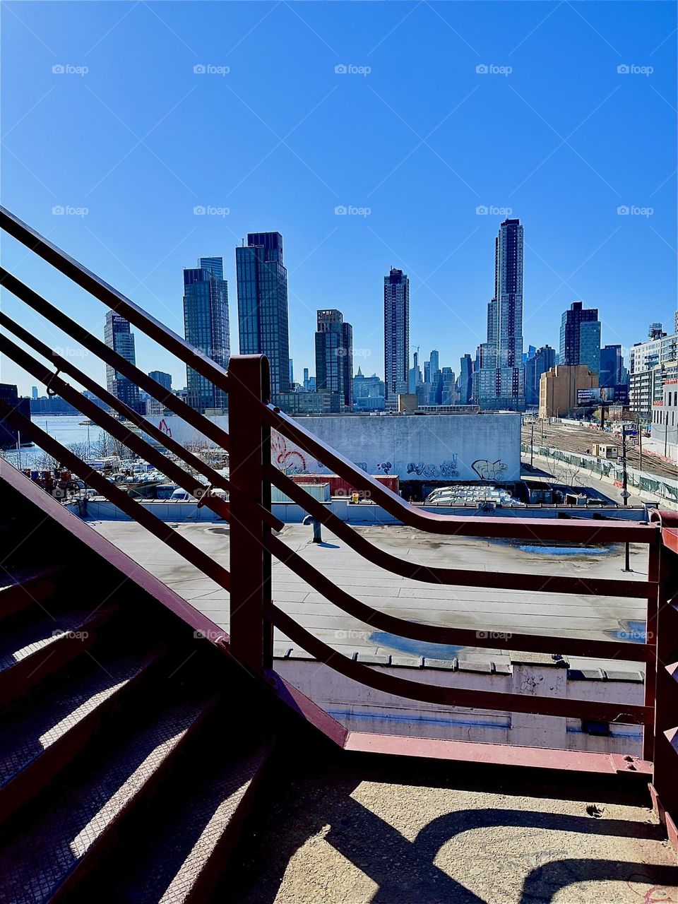 This is „Newtown Creek“ seen from the first floor up on the red metal staircase of the „Pulaski Bridge“ in LIC, Queens, NY. In the far distance across the water of the „East River“ behind LIC we see „Manhattan“. 2024. Hypnotic Productions