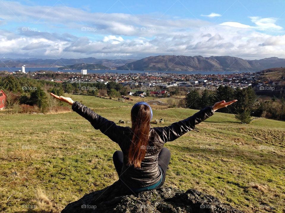 Girl enjoying the view. Daytime image of a girl sitting on a rock with the back at the camera looking towards the city of Stavanger, Norway.