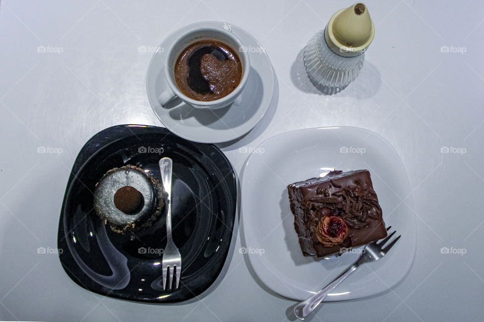 chocolate cake with raspberry mousse, black and white plates, a cup of black coffee and a sugar bowl are on the table