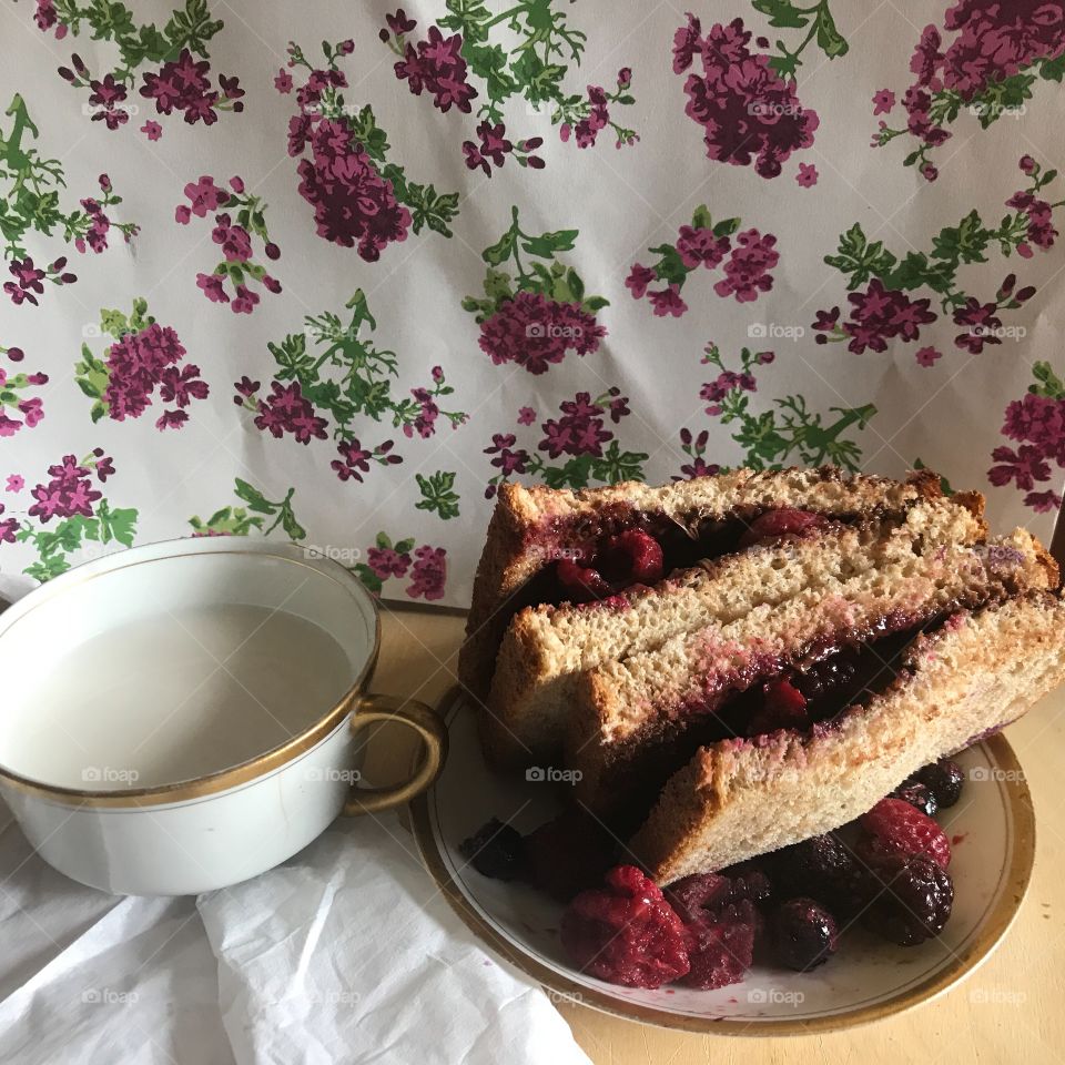 A delicious raspberry and blackberry peanut butter sandwich next to a teacup, white napkin and flora background . USA, America
