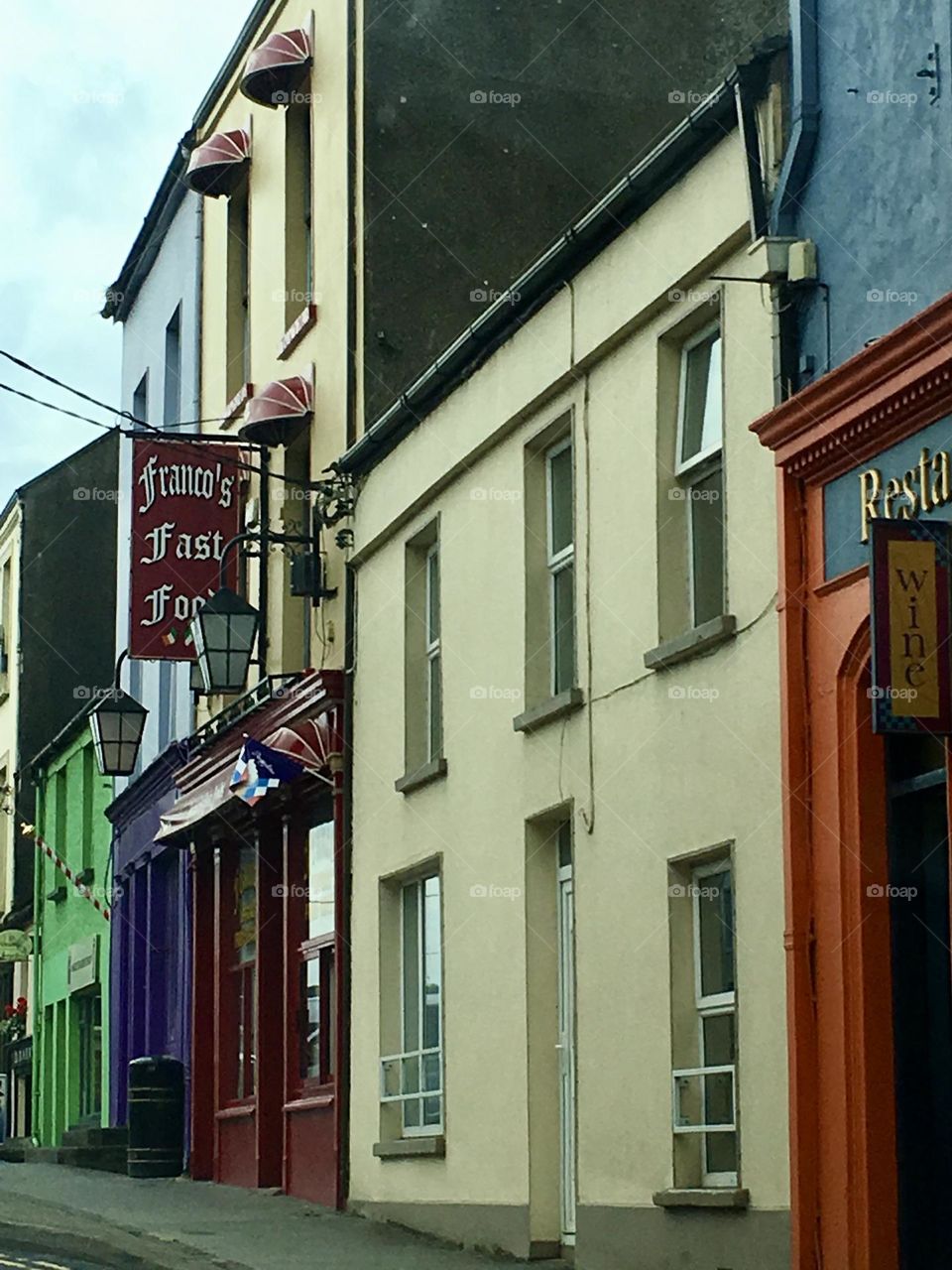 The storefronts along Main Street in Co. Clare, Ireland, are a vibrant array of colors that capture the eye. From deep, rich reds and blues to striking purples, greens, and oranges, the buildings create a lively and eclectic atmosphere.