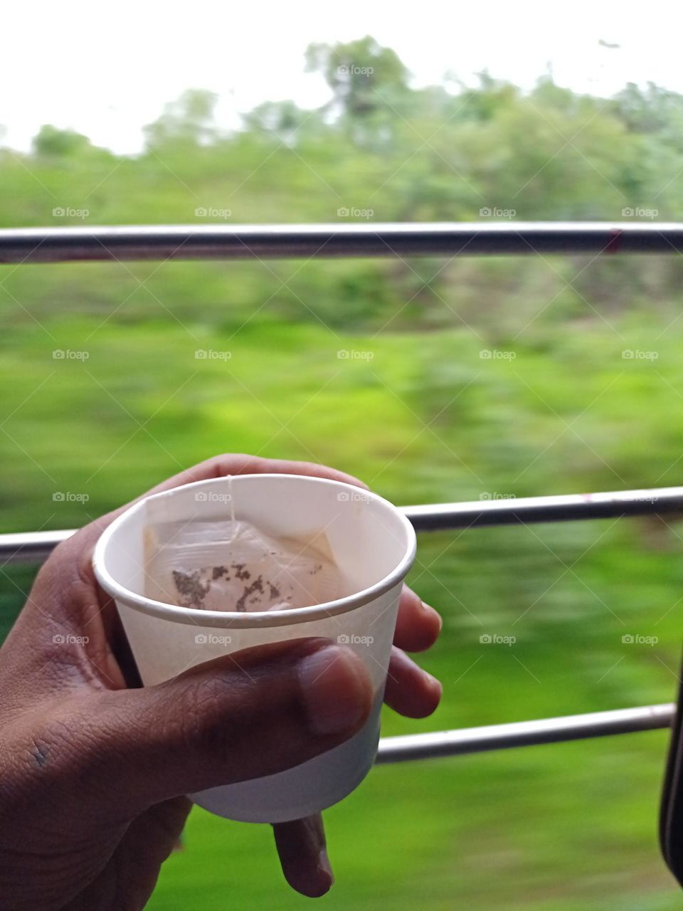Young man holding cup of tea in train journey beautiful view of train window with nice green background blur effects and metal bars on window running image