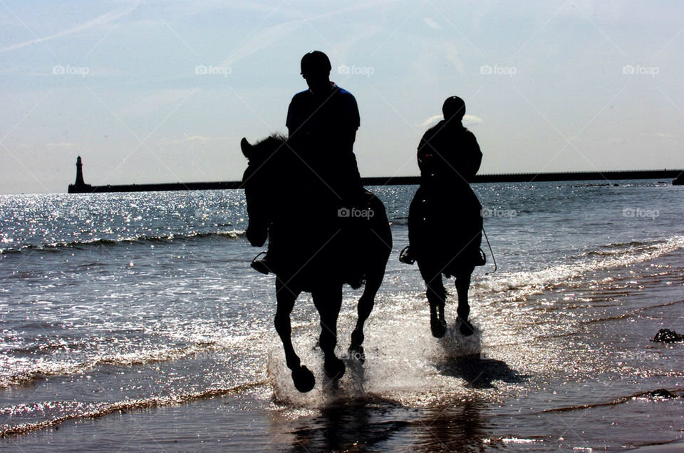 Two horse riders in silhouette on a beach with sparkling sea and a