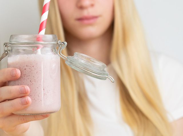 A blonde woman or girl holding a glass with strawberry milkshake or smoothie with straw 
