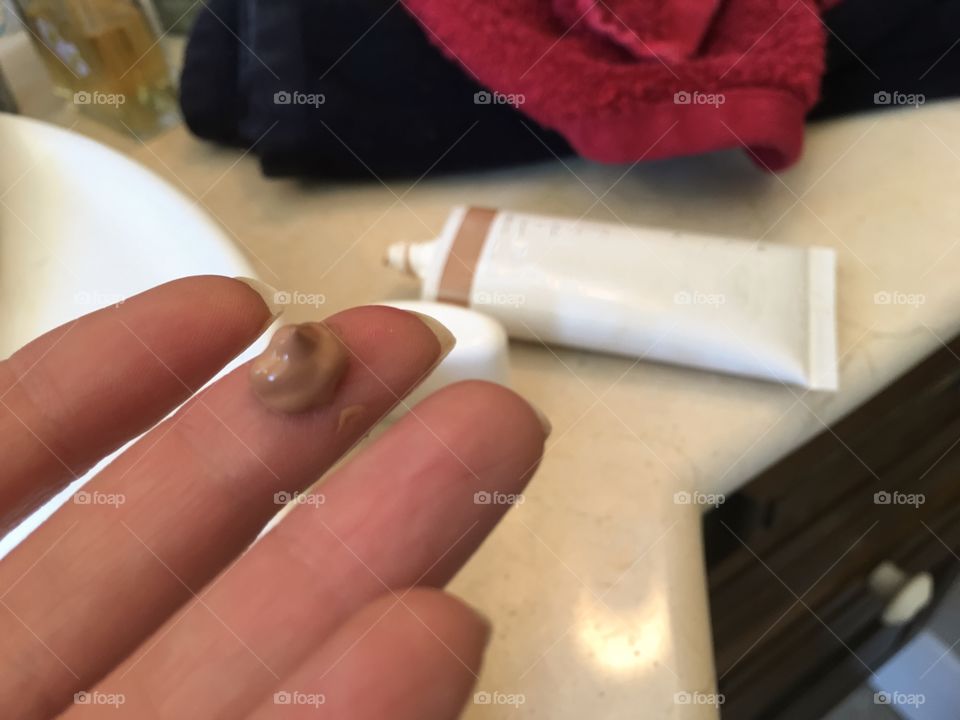 Woman applying foundation moisturizer with UV protection small quantity on finger to apply on face 