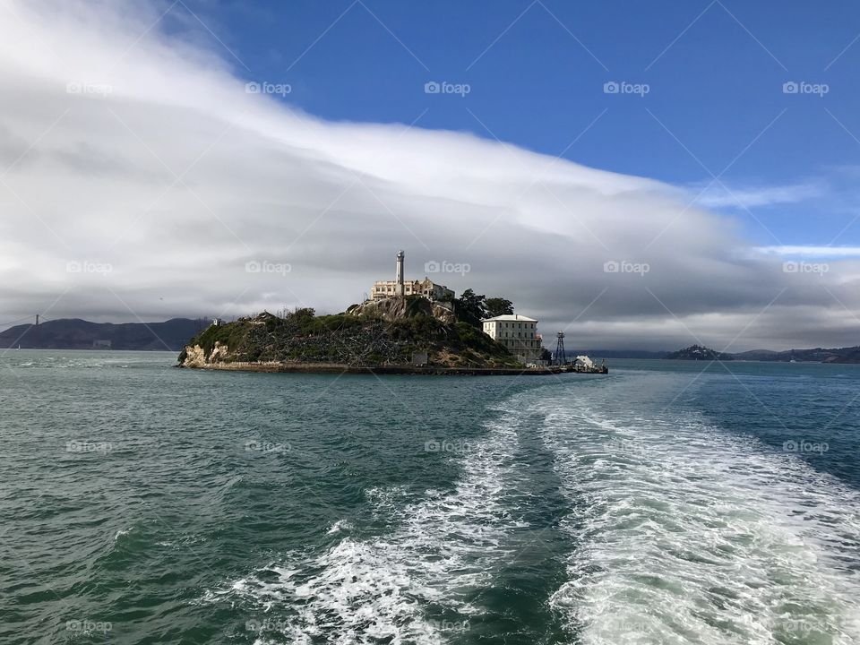 Alcatraz. On the boat / ferry leaving Alcatraz. Alcatraz in the distance from a boat with the wake in view. Small island in the distance. Prison on an island.