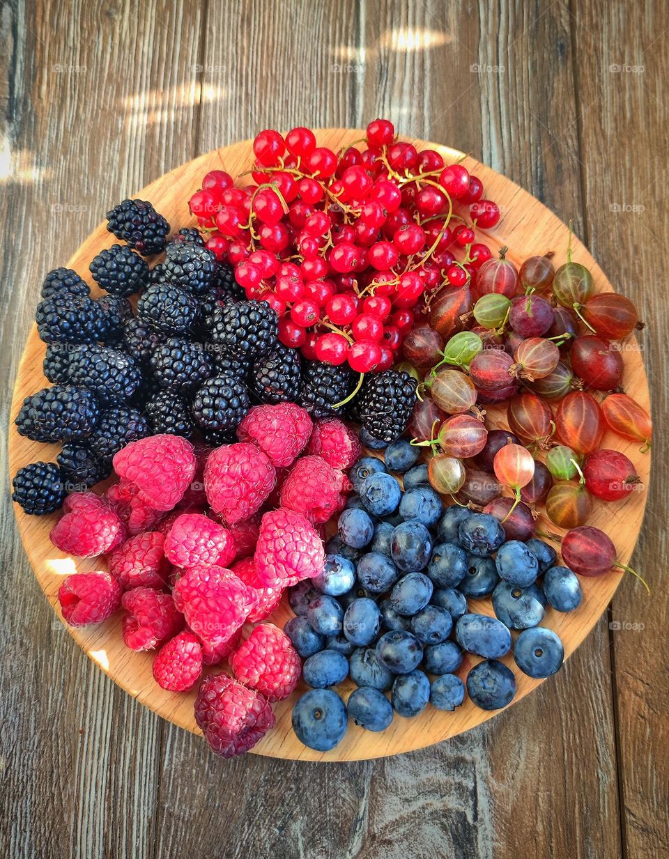 Triangles.Berries are laid out on a wooden plate in the form of triangles. Blackberry triangle, red currant triangle, brown gooseberry triangle, black blueberry triangle and red raspberry triangle