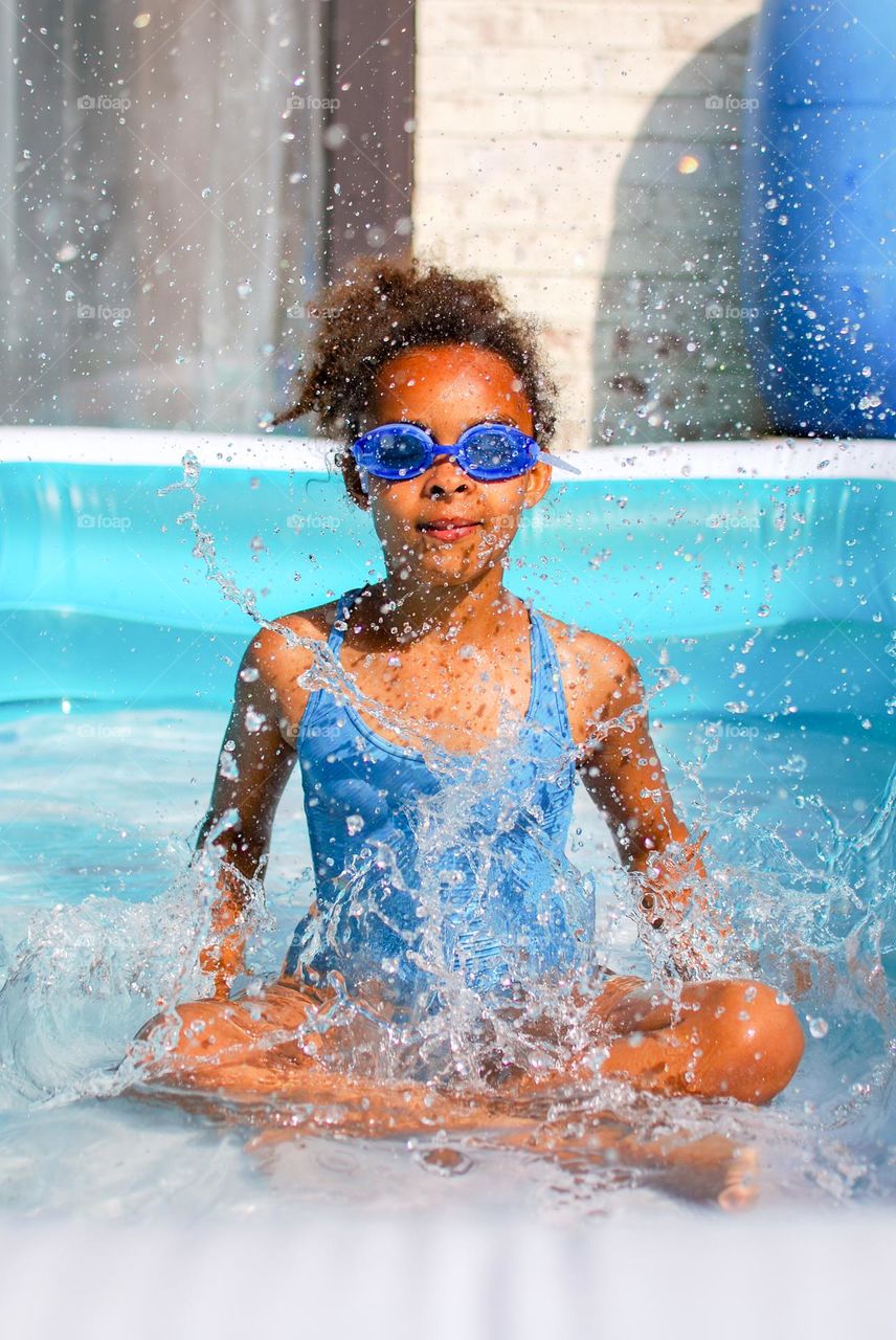 Generation Z girl / teenager girl of mixed race enjoying summer and refreshment in the water. Water splashing, blue, spats, swimming goggles, swimming suit, splash, summer time