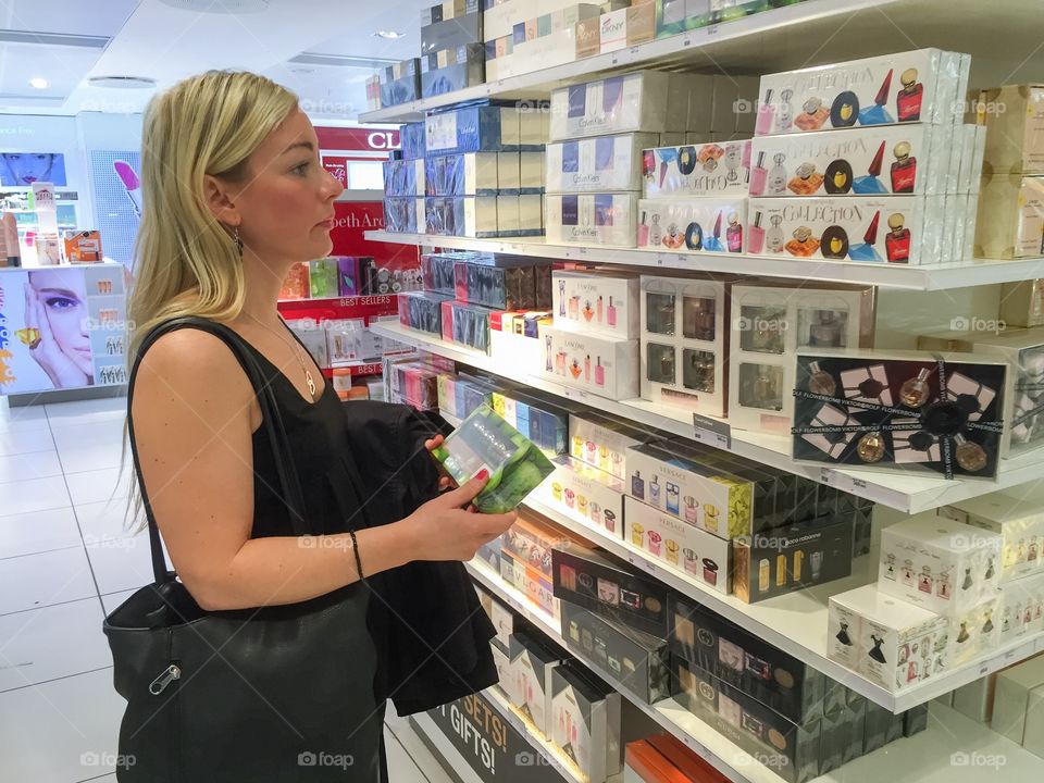 Young woman in her 30 years looking for a  perfume in a Taxfree shop at Copenhagen airport in Denmark.