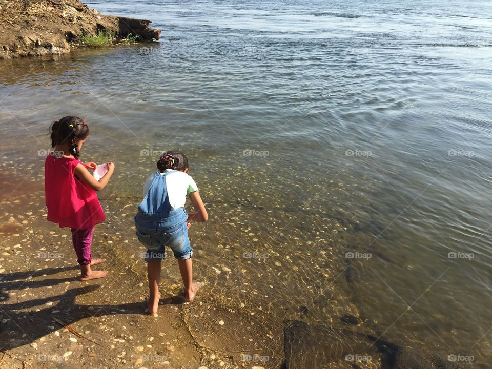  Two little girls playing and having a picnic at the Nile River beach in a sunny day. 