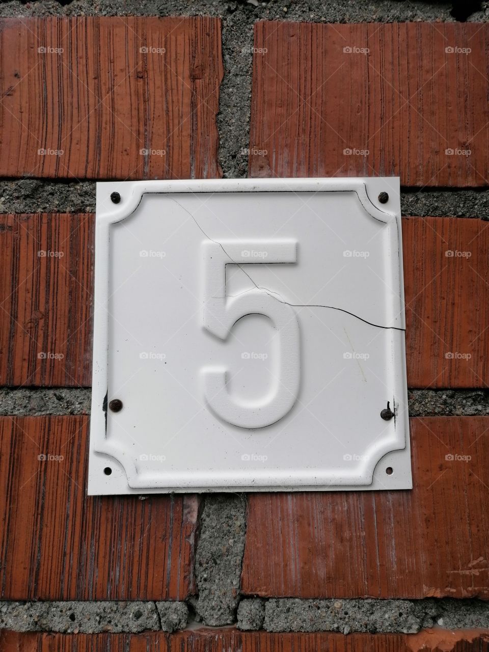 House number five 5 porcelain tile on a brick wall.