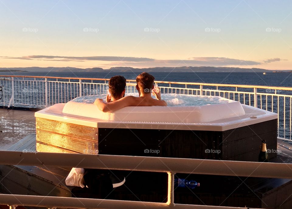 Gay couple having bath with champagne on the cruise 