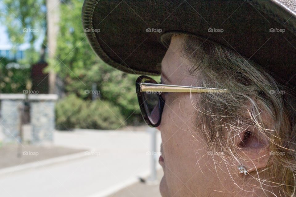 Middle aged blonde woman wearing leather cowboy hat and sunglasses side profile headshot