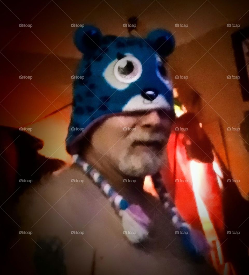 A smiling man wearing a blue stocking hat, with an animal face and blue and white tassels as part of his costume.