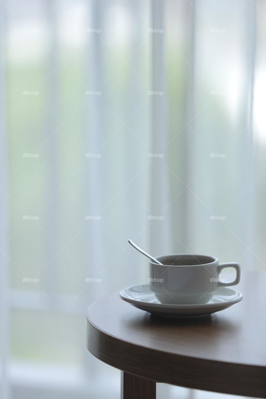 a glass of hot tea beside a charming white curtain