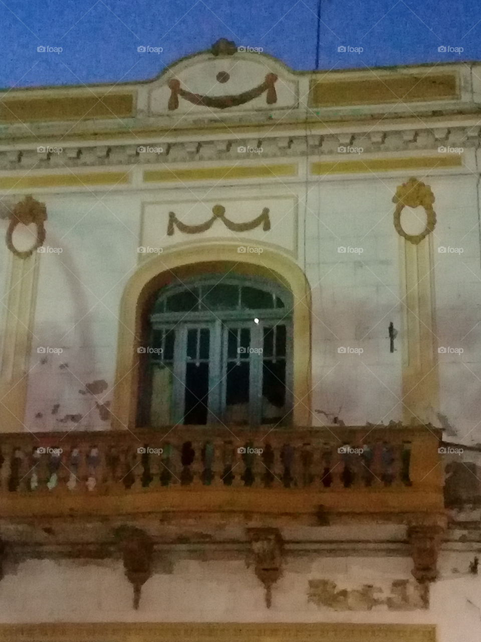 centenaria ventana con balcón y antigua celosía de madera pintada de blanco y verde y con relieves decorativos en los laterales de la pared y sobre el techo