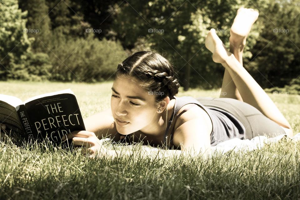 Beautiful young woman is reading a book laying in the grass
