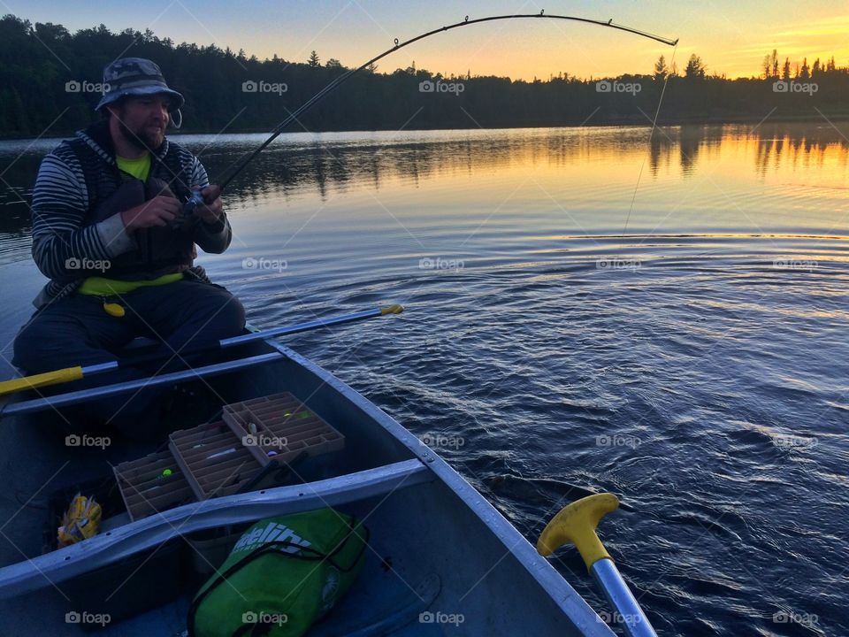 Mature man doing fishing in lake during sunset