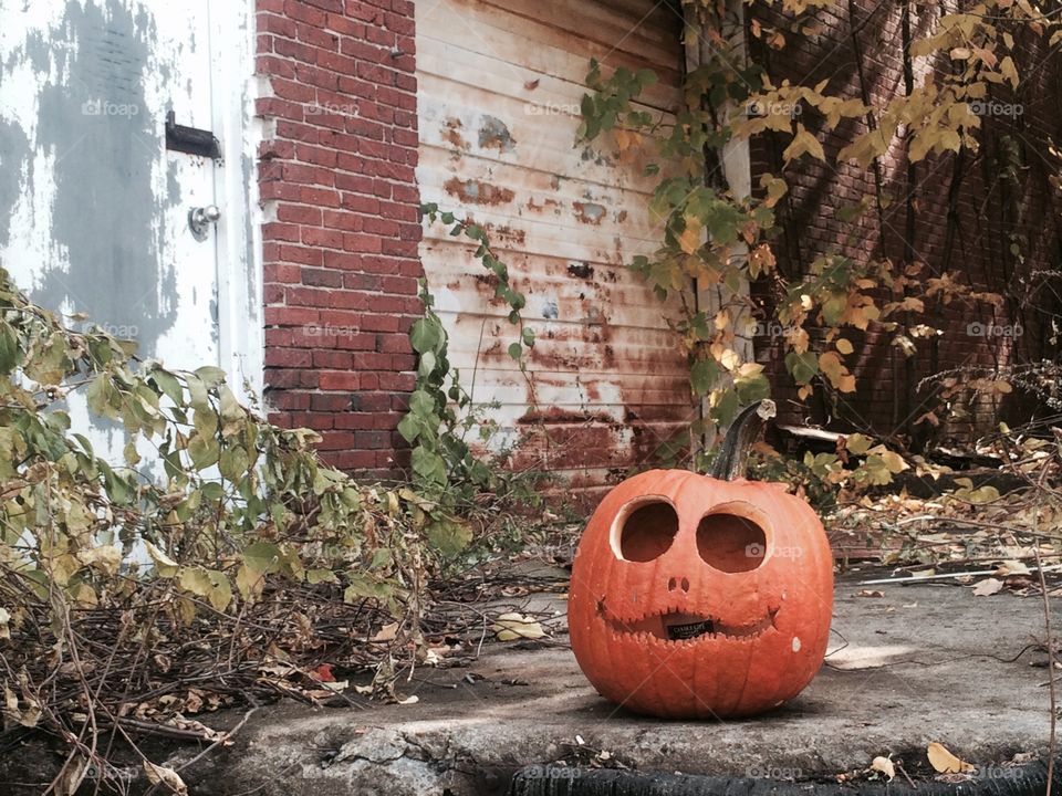 Creepy jack'o lantern . A jack'o lantern sits out front of an abandon  warehouse. 
