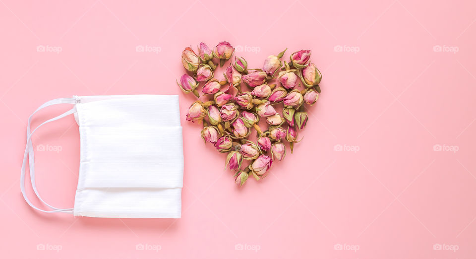 Abstract composition of a handmade protective mask and shape of heart made by roses buds. Concept of prevention and fight against a new coronavirus COVID-19. Hope and life.