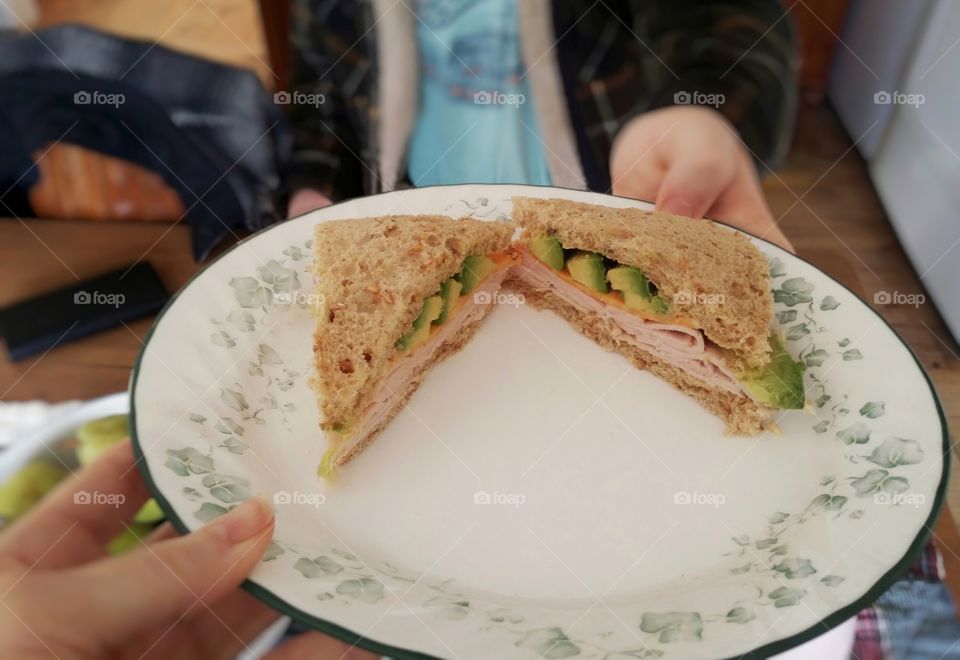 A woman handing a man a plate with a turkey avocado cheese dijon mustard on whole grain wheat bread sandwich on it